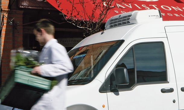 Photo of a man unloading flowers from a van in front of a store.